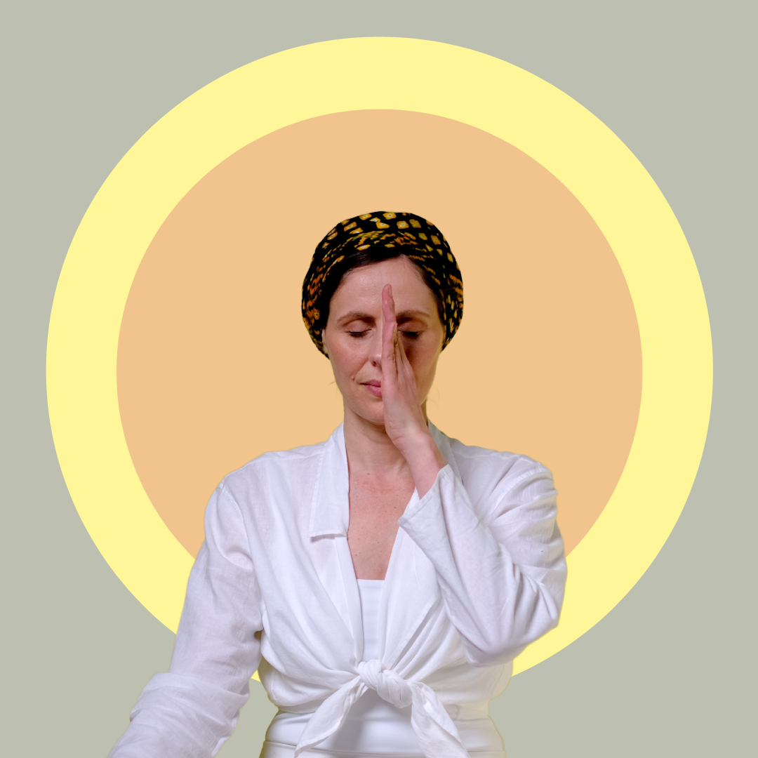 A woman wearing a white top and patterned headscarf practices alternate nostril breathing, sitting with eyes closed in front of a large yellow and orange circular background.